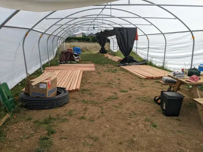 Photo de la serre encore en travaux, avec des planches de bois et des baches